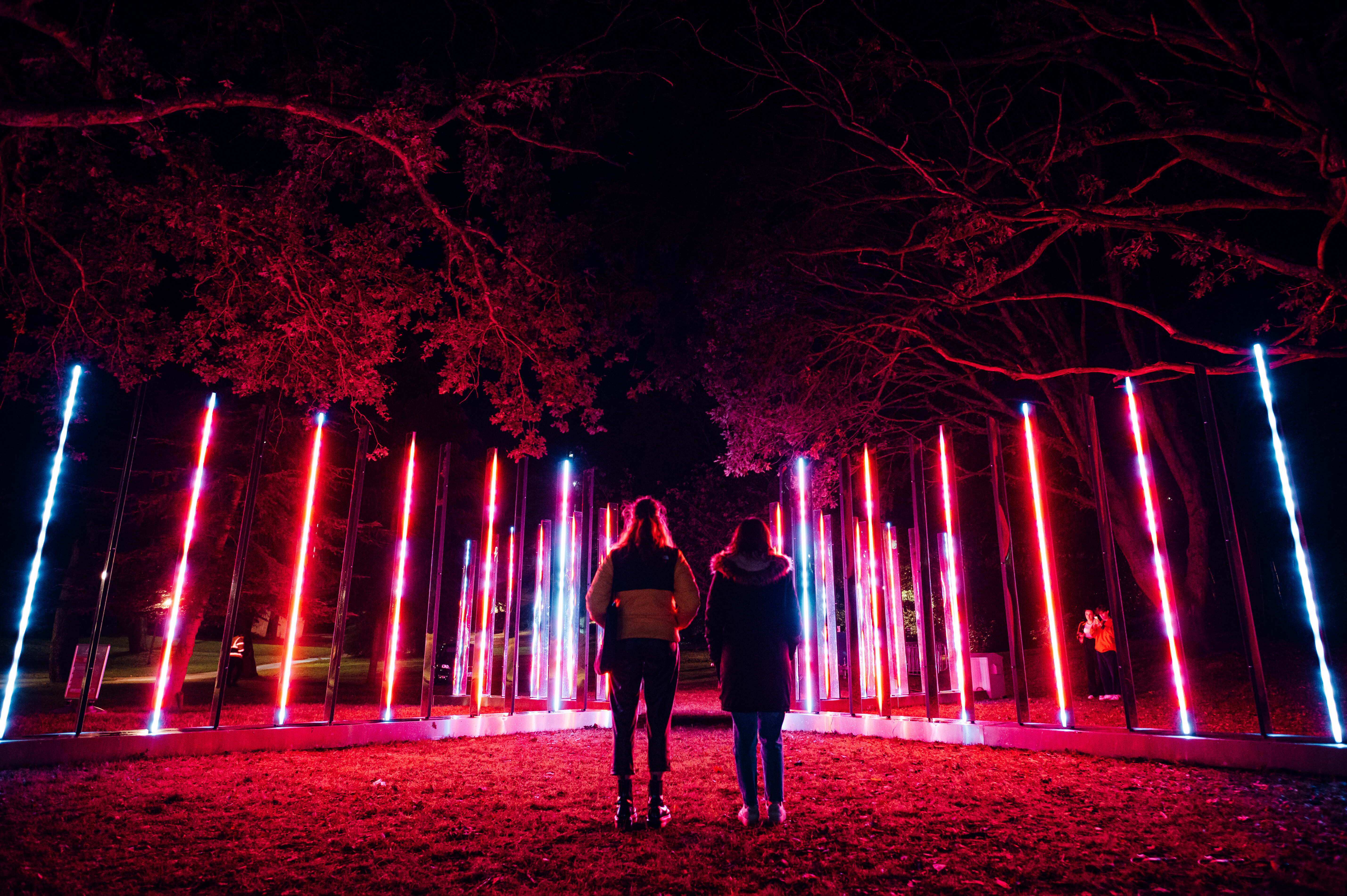 Two people watching the light display showing pink lights at Bournemouth Arts by the Sea Festival