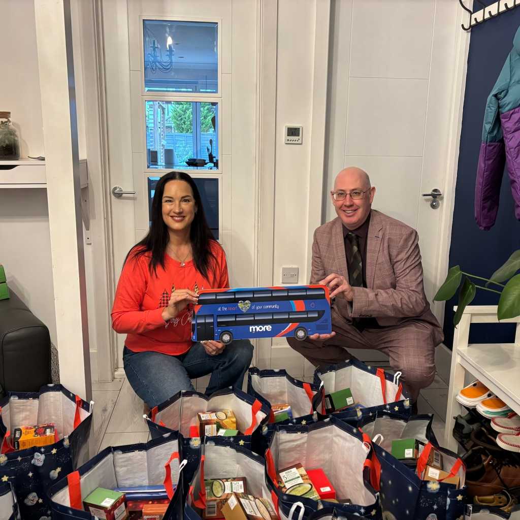 Two people holding a More bus cut out crouched behind care packages