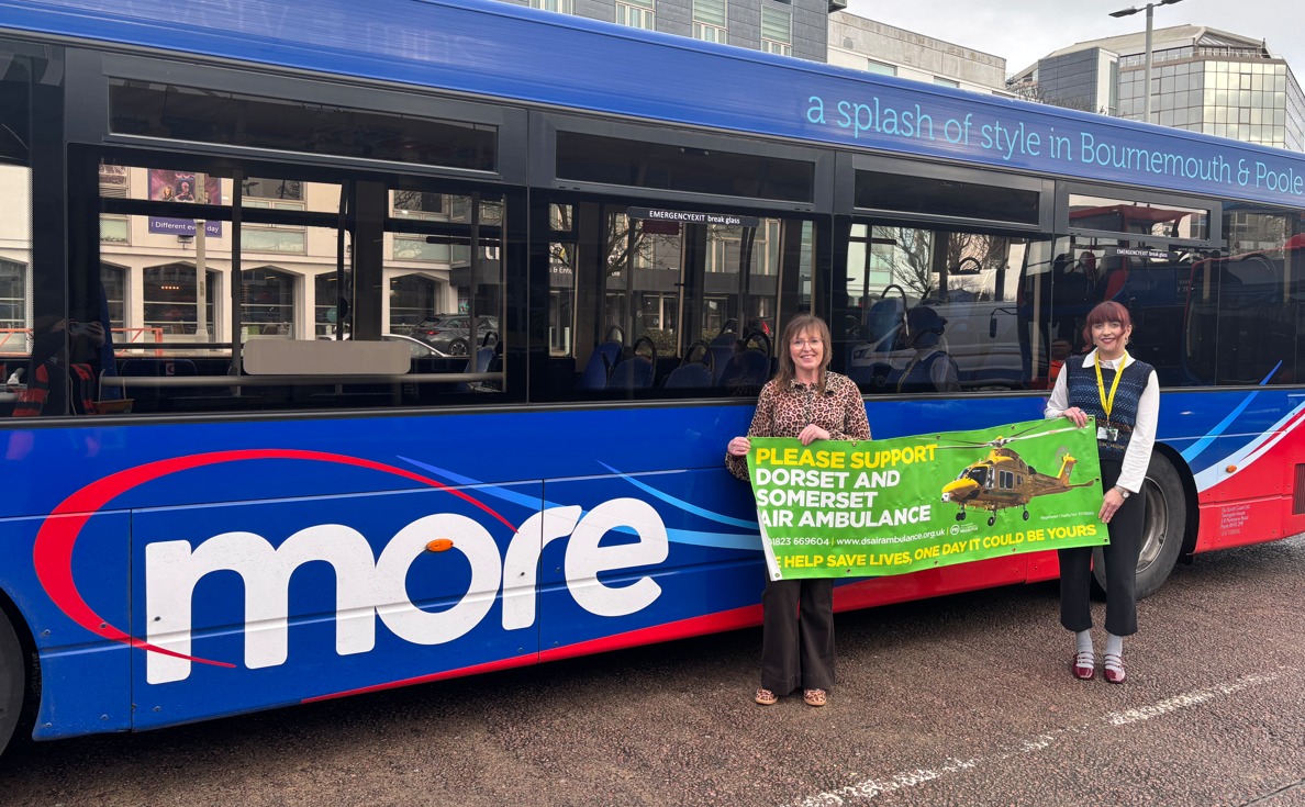 Two people stood next to a Morebus holding a Dorset and Somerset Air ambulance banner