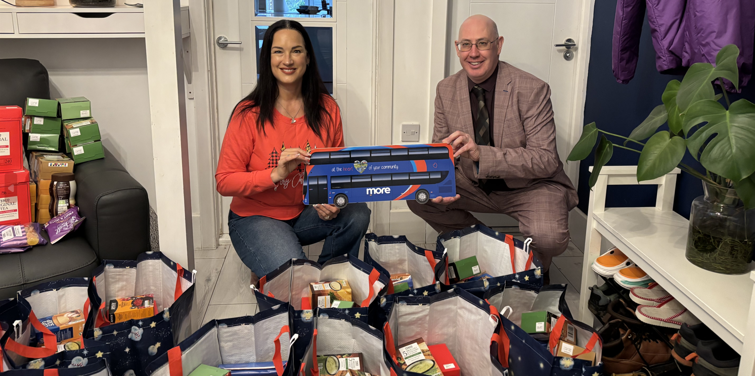 Two people holding a cut out of a bus behind food packages