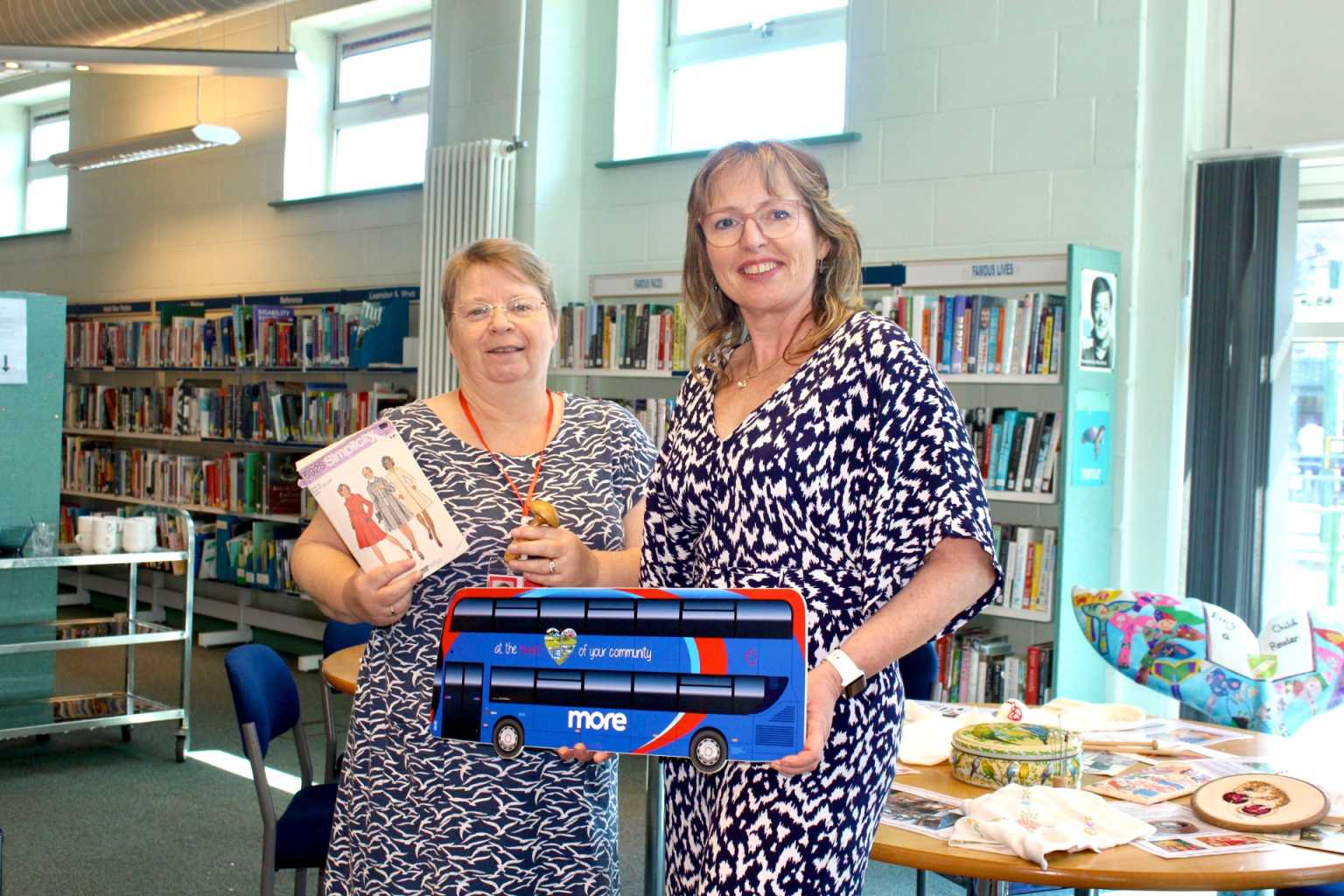Two ladies in a library holding a More bus cut out